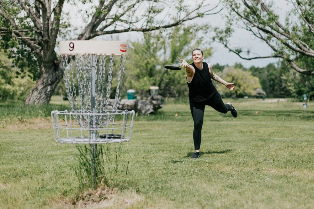 Femme en approche finale du panier au disc golf dans un parcours boisé