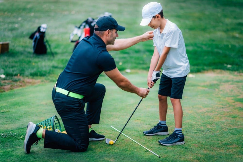 Coach de golf spécialisé avec son élève expliquant comment débuter le golf enfant