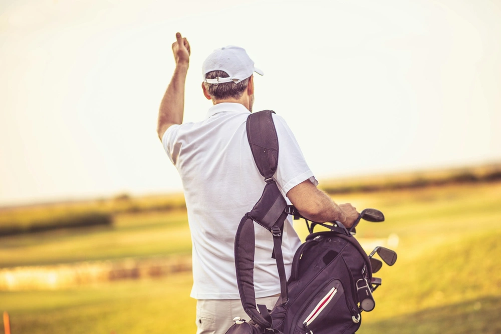 Golfeur portant son sac au coucher du soleil — golf bien-être social et longévité