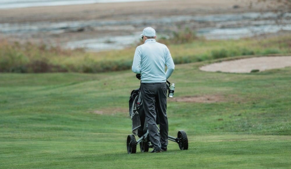 Golfeur ayant mal au dos au golf utilisant un chariot pour porter son matériel sur le parcours