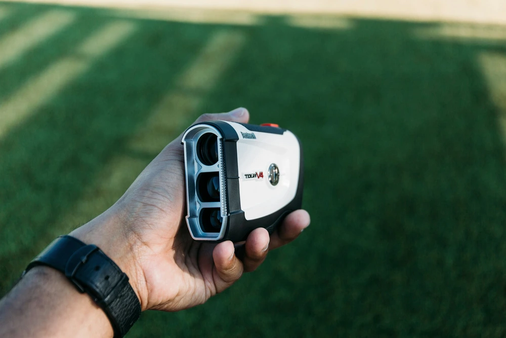 Télémètre golf Bushnell Tour V4 tenu en main sur green — précision laser et verrouillage drapeau