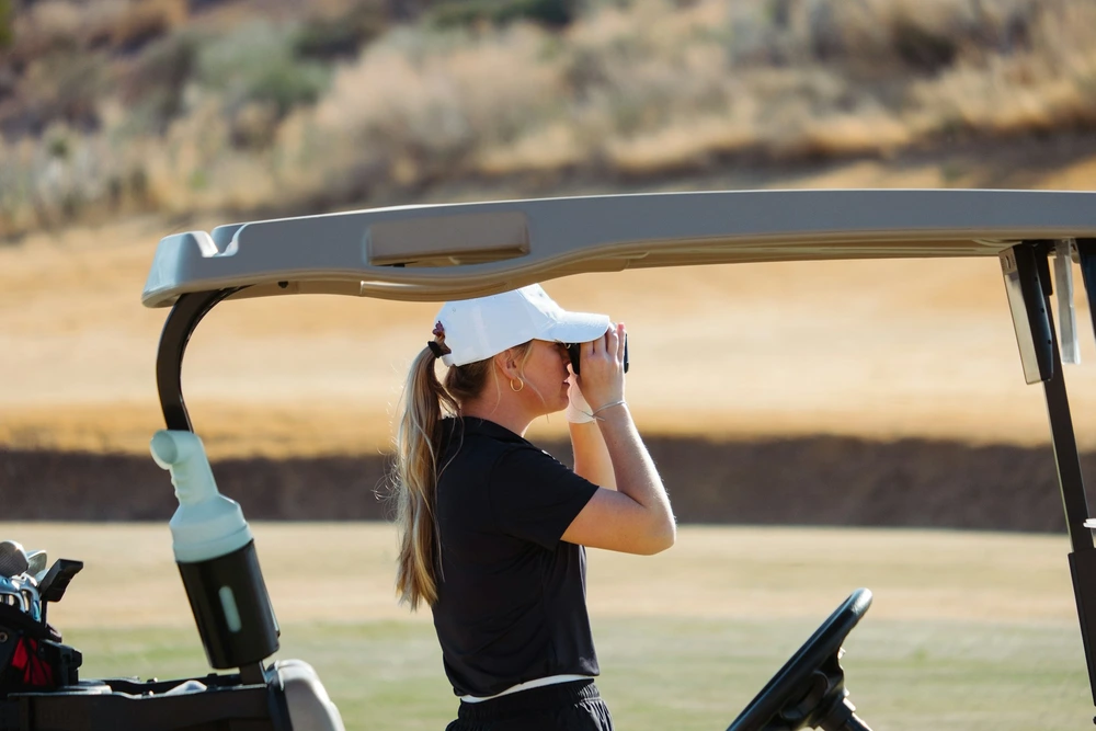 Golfeuse utilisant un télémètre laser depuis un buggy — mesure de distance au drapeau sur parcours