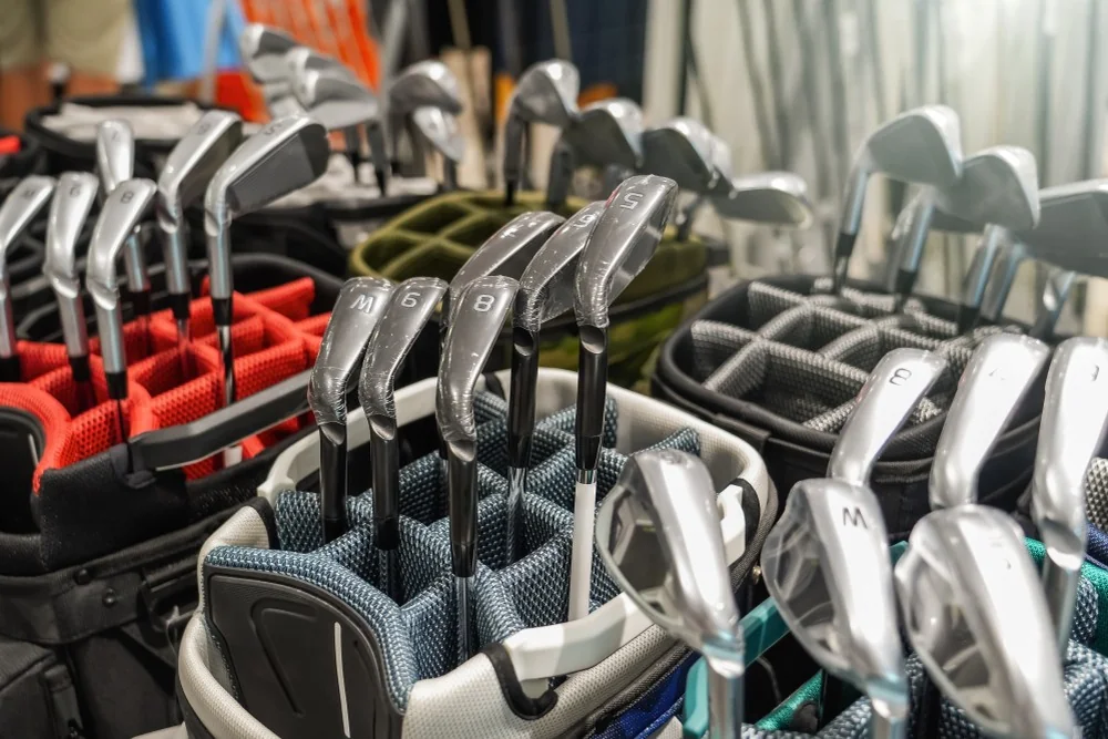 Rayon de fers de golf dans un pro-shop avec sacs de clubs alignés pour illustrer l'achat neuf ou occasion