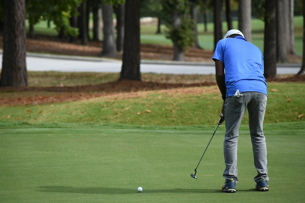 Golfeur de dos exécutant un mouvement pendulaire au putting initié depuis les épaules
