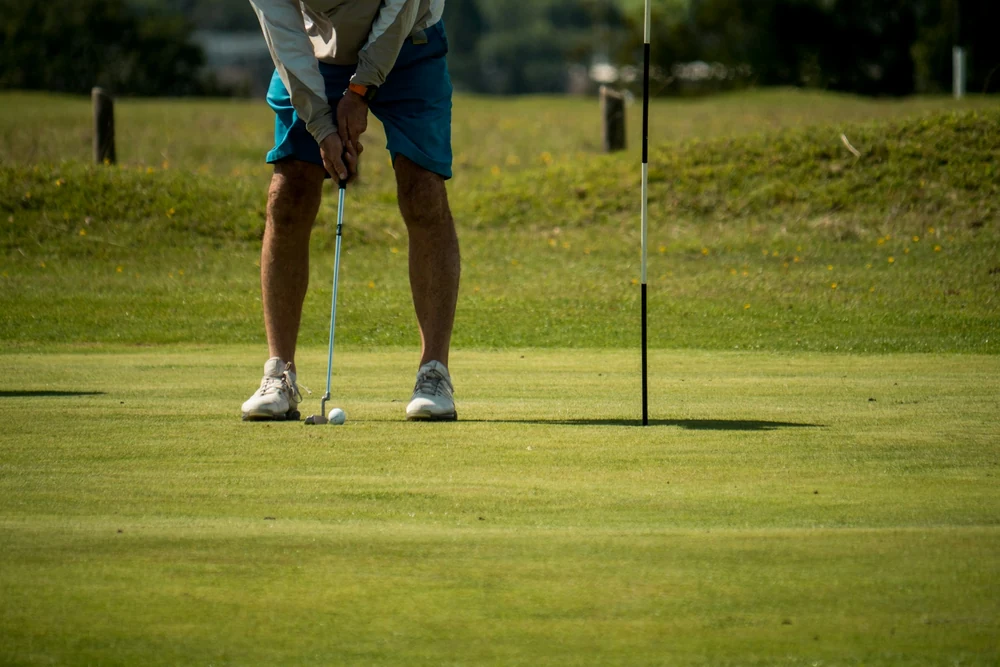 Golfeur en posture d'adresse au putting, jambes stables et putter en main face au drapeau