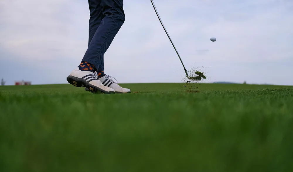 Golfeur en mouvement frappant une balle de golf sur un parcours herbeux