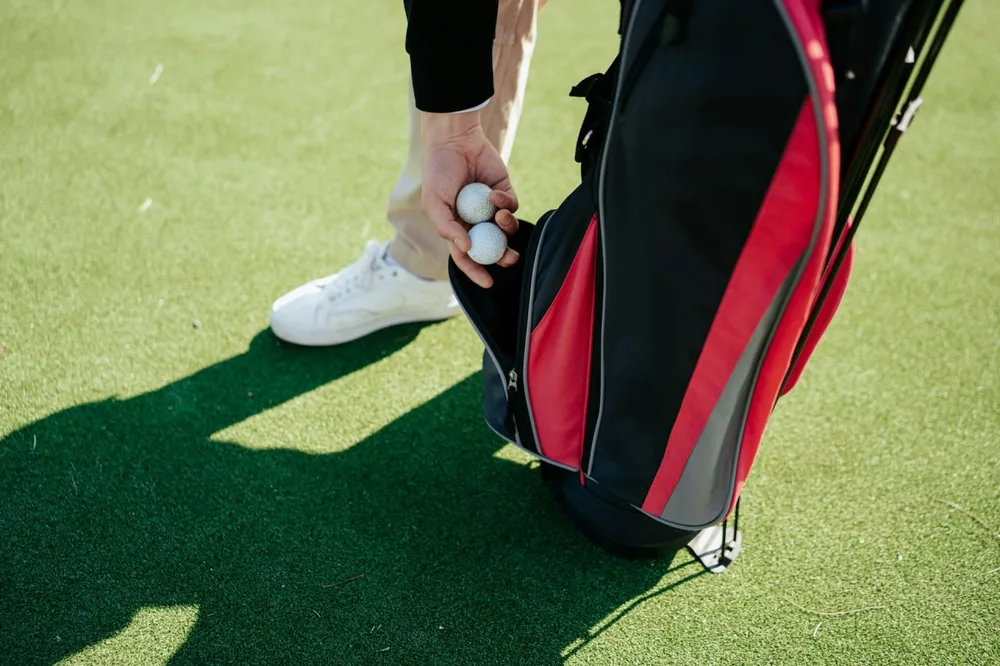 Main tenant deux balles de golf près d'un sac rouge et noir sur un green.