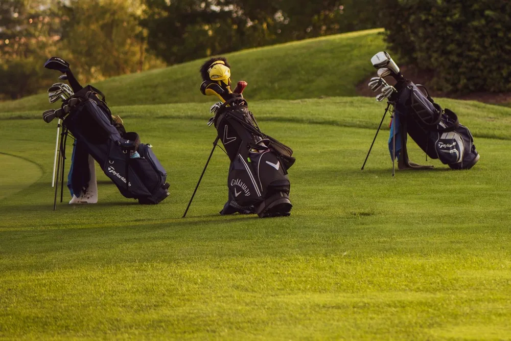 Trois sacs de golf a trepied poses sur le fairway pres d un green.