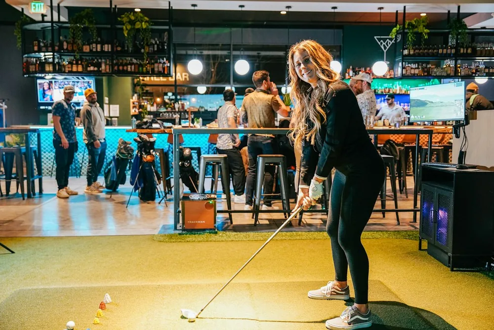 Femme souriante se préparant à frapper une balle de golf dans un simulateur intérieur