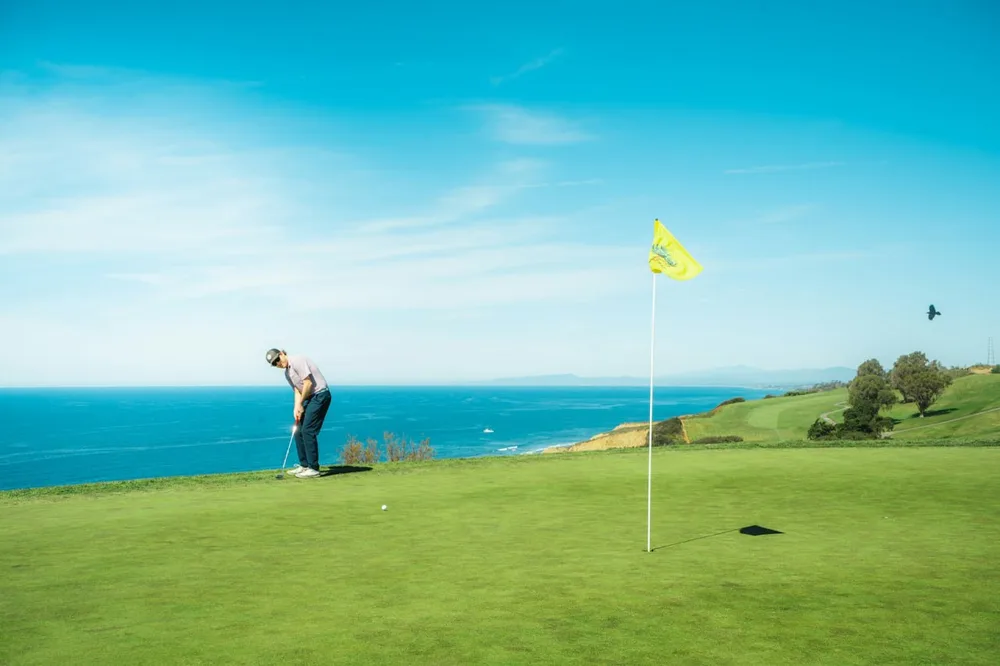 Golf vent : un golfeur se prépare à jouer sur un parcours côtier près d'un drapeau jaune.