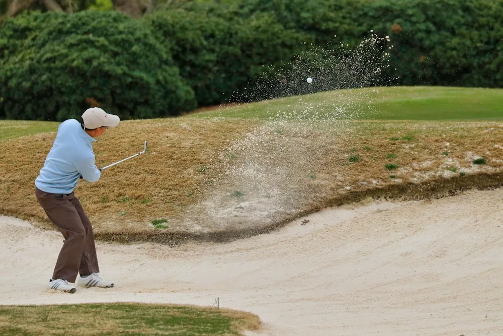Golfeur en tenue légère effectuant une sortie de bunker sur un pitch and putt