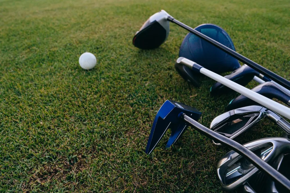 Plusieurs clubs de golf aux formes de têtes différentes posés sur l'herbe à côté d'une balle pour comprendre les noms des clubs de golf.
