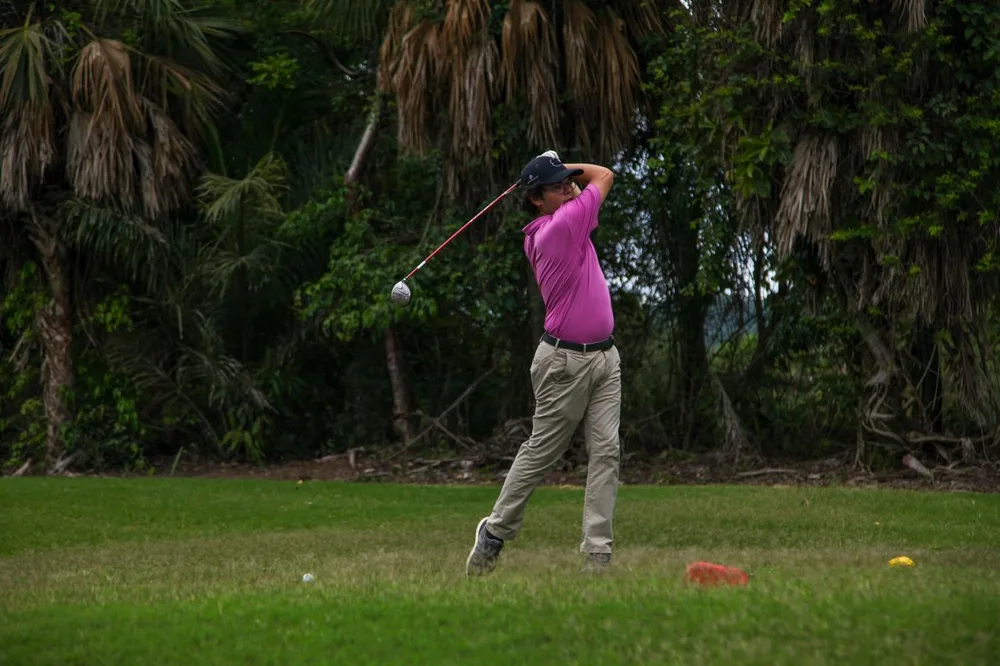 Golfeur en polo rose en fin de swing avec un bois de parcours, près des repères de départ.