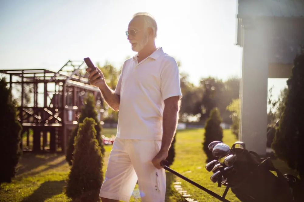Espace licencié ffgolf : golfeur âgé consultant son téléphone en marchant avec son sac